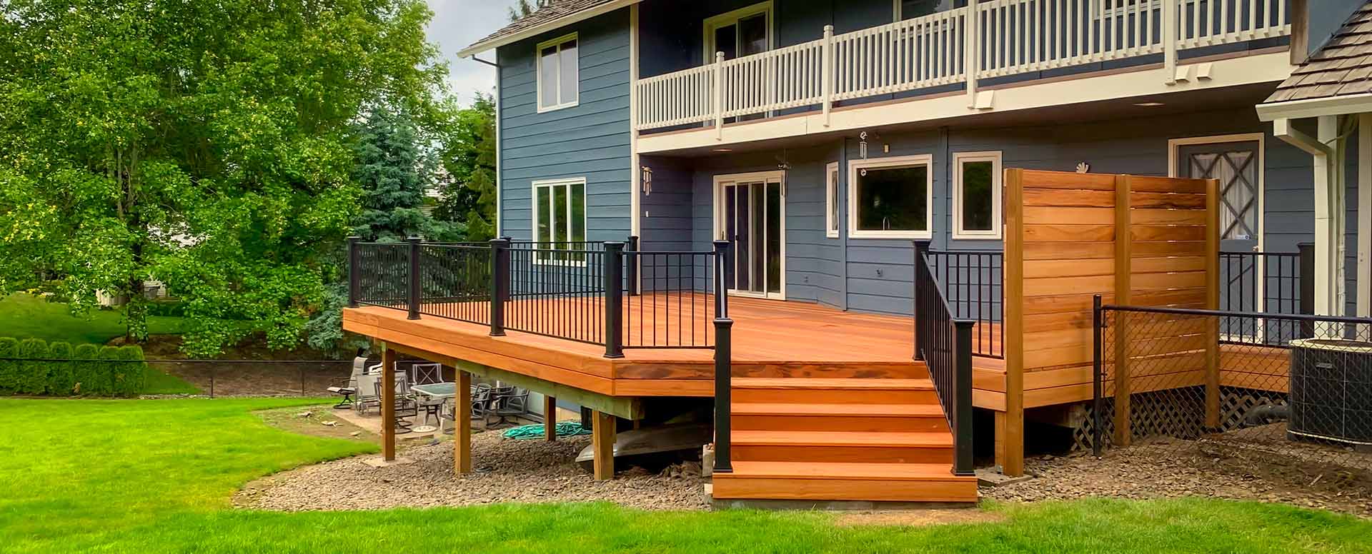 The backside of a blue house with a new deck on the first floor with black metal railing.
